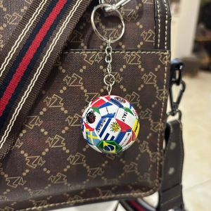 Detail eines Fußball-Schlüsselanhängers mit Flaggen an einer braunen gemusterten Tasche