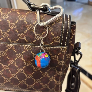 Mini globe keychain with world map hanging on a brown patterned leather bag