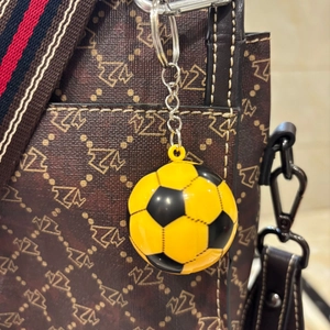 Dettaglio portachiavi da calcio giallo e nero appeso a una borsa con motivi marroni