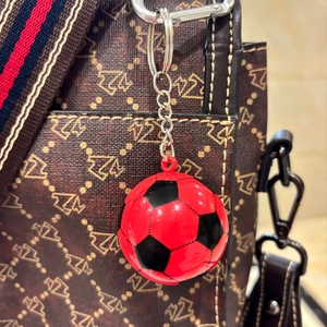 Dettaglio di un portachiavi da calcio rosso e nero appeso a una borsa marrone a motivi