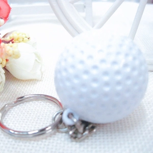 Detail of a white golf ball keychain featuring realistic textured dimples and silver metal ring