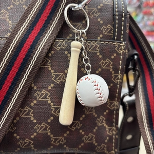 Miniature baseball and wooden bat keychain hanging on a brown patterned leather bag