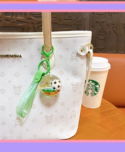 Detail of soccer liquid quicksand keychain with green strap on a bag accessory