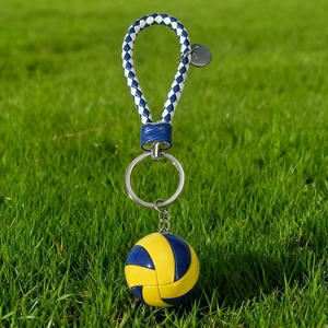 Blue and yellow volleyball keychain with woven leather strap on a lush green lawn