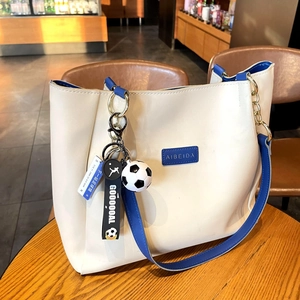 Close-up of a football keychain pendant with GOOOOAL ribbon attached to a cream tote bag
