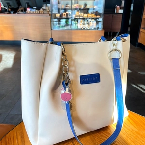 Détail d'un cabas en cuir crème avec bordure bleue, chaîne dorée et breloque lapin rose