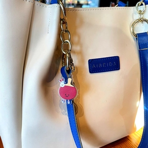 Gros plan d'un porte-clés raquette de ping-pong rouge attaché à un sac à main beige en cuir