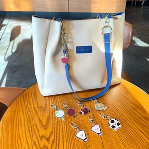 Sac fourre-tout blanc orné de divers porte-clés de sport comme le foot et le basket