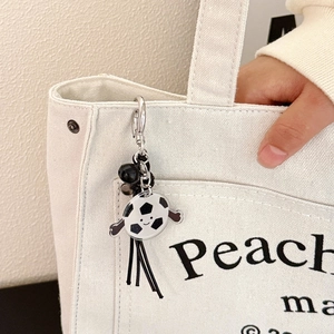 Gros plan du pendentif ballon de foot avec pompon noir accroché à un sac en toile