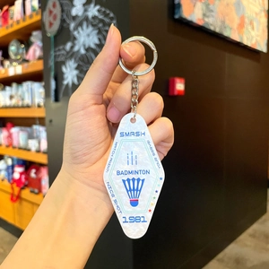 Detail of rhombic badminton keychain with blue Smash text on white pearly acrylic
