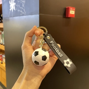 Détail du porte-clés football avec ballon noir et blanc, anneau doré et lanière en caoutchouc