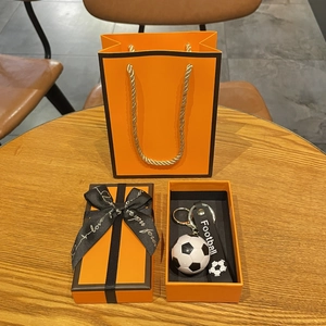 Détail du porte-clés football avec lanière en cuir dans sa boîte cadeau orange et sac