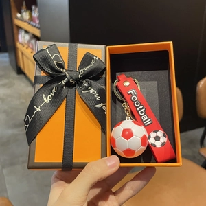 Gros plan d'un porte-clés football rouge avec dragonne dans une boîte cadeau orange