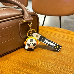 Close-up of a cartoon soccer keychain with headphones hanging on a brown leather bag