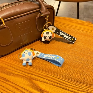 Close-up of a cartoon football keychain with headphones on a leather designer handbag