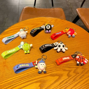 Set of seven cartoon sports ball keychains with silicone straps on a wooden table