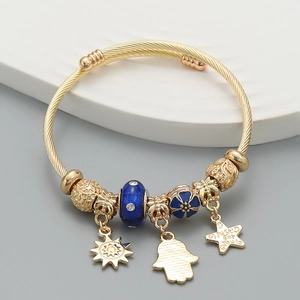 Detail of bohemian gold spiral bangle with sun, hand, and star charms plus blue bead