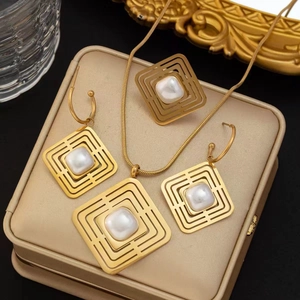 Détail de parure bijoux géométrique dorée avec cadres carrés et perles sur un coffret