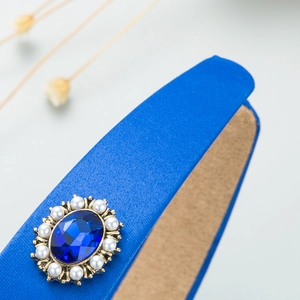 Detail of blue satin headband featuring a large sapphire gem and pearl embellishments