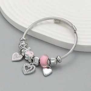 Silver-tone cable bangle featuring pink heart pendants and crystal beads on a tray