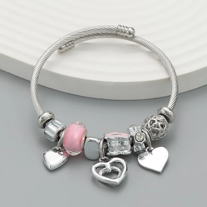 Silver beaded bracelet with pink charms and heart pendants on a stylish round display