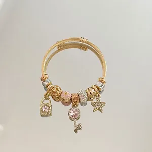 Macro view of gold woven steel bracelet featuring pink zircon stars and key charms