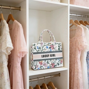 Floral print canvas tote bag with LUCKY GIRL embroidery displayed in a white wardrobe