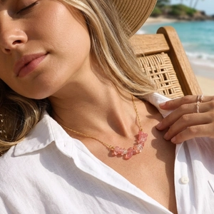 Close-up of irregular pink natural stone necklace with gold chain in a beach setting