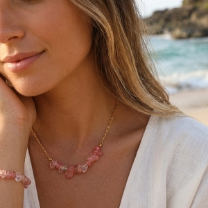 Close-up of pink crystal beads on a golden chain necklace worn on a beach setting