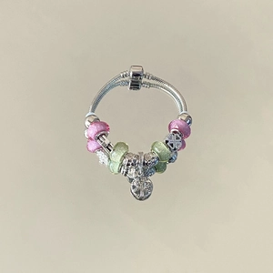 Detailed macro of a snake chain bracelet with pink and green glass beads and metal charms