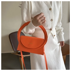 Detail der leuchtend orangefarbenen Handtasche mit großem Rundgriff und Markenschrift