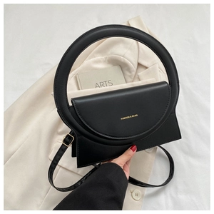 Detail der schwarzen PU-Leder Handtasche mit Rundgriff und Goldschnalle auf beigem Blazer