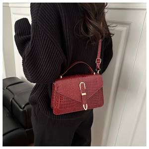 Detail of dark red crocodile textured handbag featuring a gold horseshoe buckle closure
