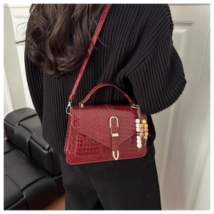 Detail view of burgundy crocodile pattern handbag with golden buckle and beads