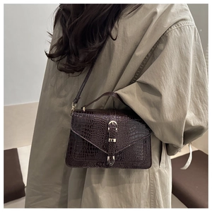 Deep brown crocodile texture crossbody bag detail on model with metallic buckle closure
