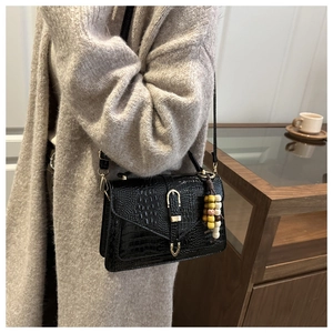 Detail of black crocodile texture shoulder bag with colorful wooden beads and metal lock