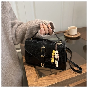 Close-up of black crocodile pattern leather bag with gold U-buckle and beaded charm