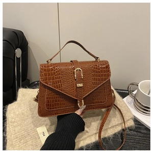 Detail of brown crocodile pattern handbag with golden horseshoe buckle and textured leather