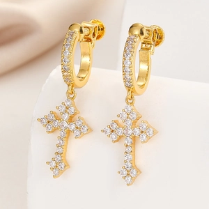 Golden hip hop cross earrings with white cubic zirconia pavé stones on a satin background