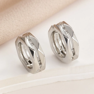 Close-up of silver geometric huggie earrings with a polished multi-faceted surface