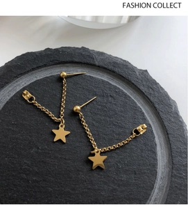Détail de boucles d'oreilles étoile avec chaîne dorée sur surface en pierre