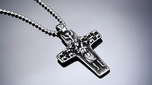 Macro shot of silver vintage cross pendant with embossed figures and a classic ball chain