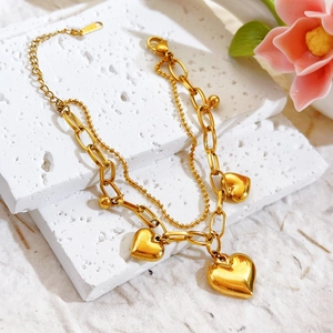 Gold double-layered stainless steel bracelet with heart pendants on a white stone background