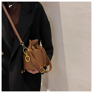 Detail of a brown leather bucket bag with drawstring closure and golden hardware charm