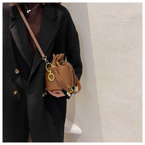 Detail of brown bucket bag with gold octagon charm and drawstring on a wool coat