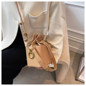 Model wearing apricot drawstring bucket bag with gold octagonal hardware detail