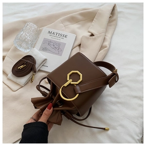 Detail of dark brown leather bucket bag with gold geometric metal clasp and drawstring closure