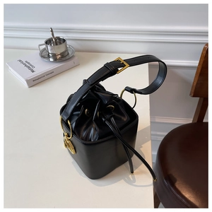 Detail of black drawstring bucket bag with gold hardware and adjustable strap on desk