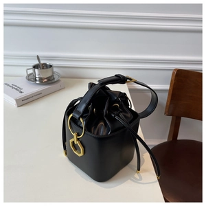 Macro view of matte black bucket bag with golden circular hardware and drawstring closure