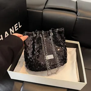 Close-up of a black sequined bucket bag featuring a silver chain strap and metal logo plate